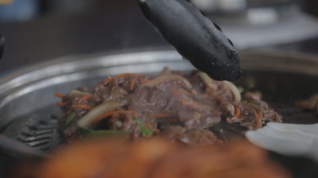 Marinated beef bulgogi being tossed on a grill with black tongs